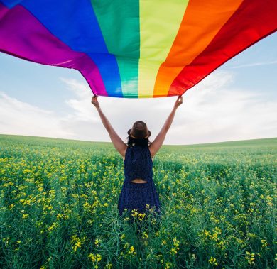 Woman holding the Gay Rainbow Flag on a green meadow outdoors. Happiness, freedom and love concept for same sex couples.